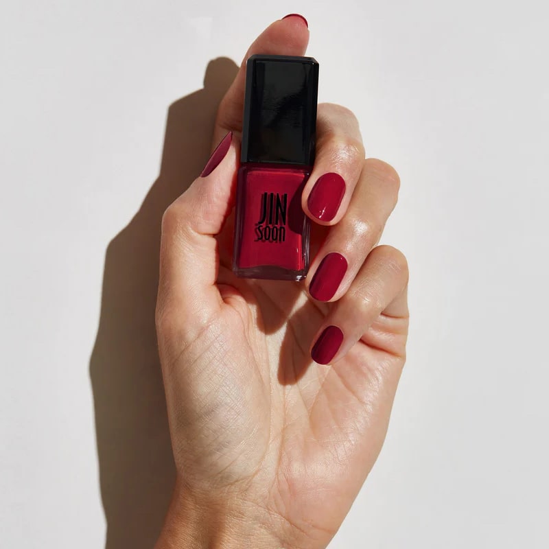 Model with light skin tone wearing and holding bottle of JINsoon Nail Lacquer - Coquette