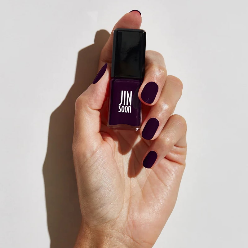 Model with light skin tone wearing and holding bottle of JINsoon Nail Lacquer - Risque