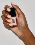 Model with dark skin tone wearing and holding bottle of JINsoon Nail Lacquer - Nostalgia