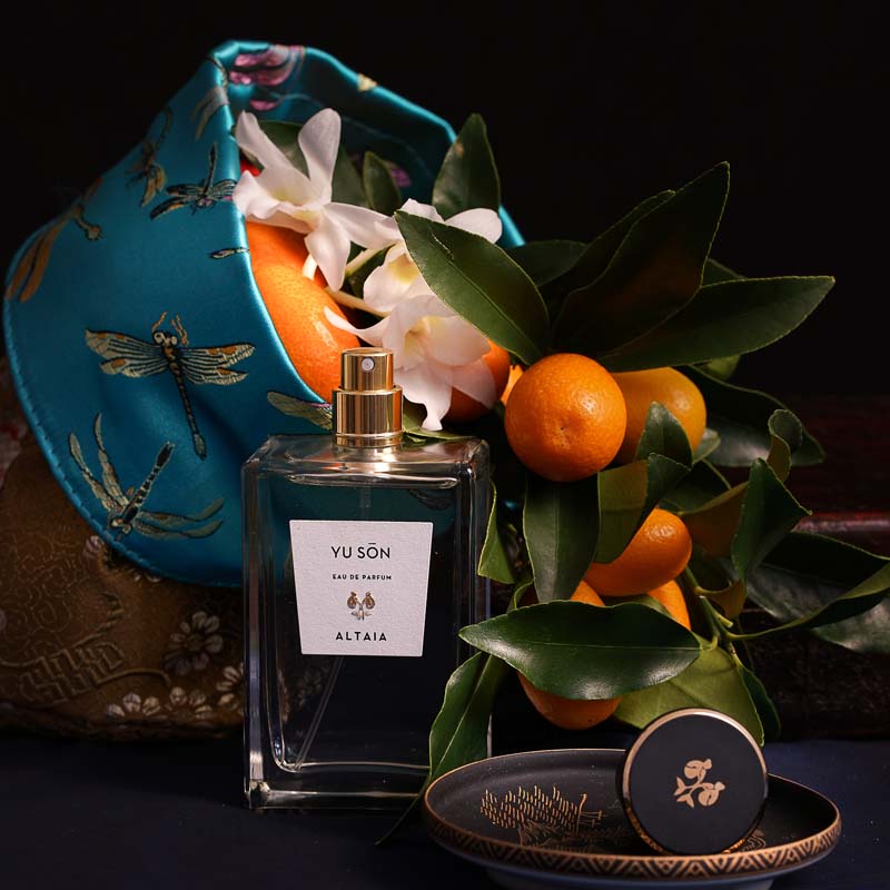 Beauty shot of ALTAIA Yu Son Eau de Parfum with embroidered basket in the background filled with oranges and white flowers