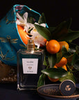 Beauty shot of ALTAIA Yu Son Eau de Parfum with embroidered basket in the background filled with oranges and white flowers