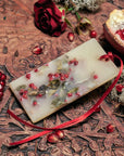 Lifestyle shot of Santa Maria Novella Melograno Scented Wax Tablet with pomegranate and red rose in the background