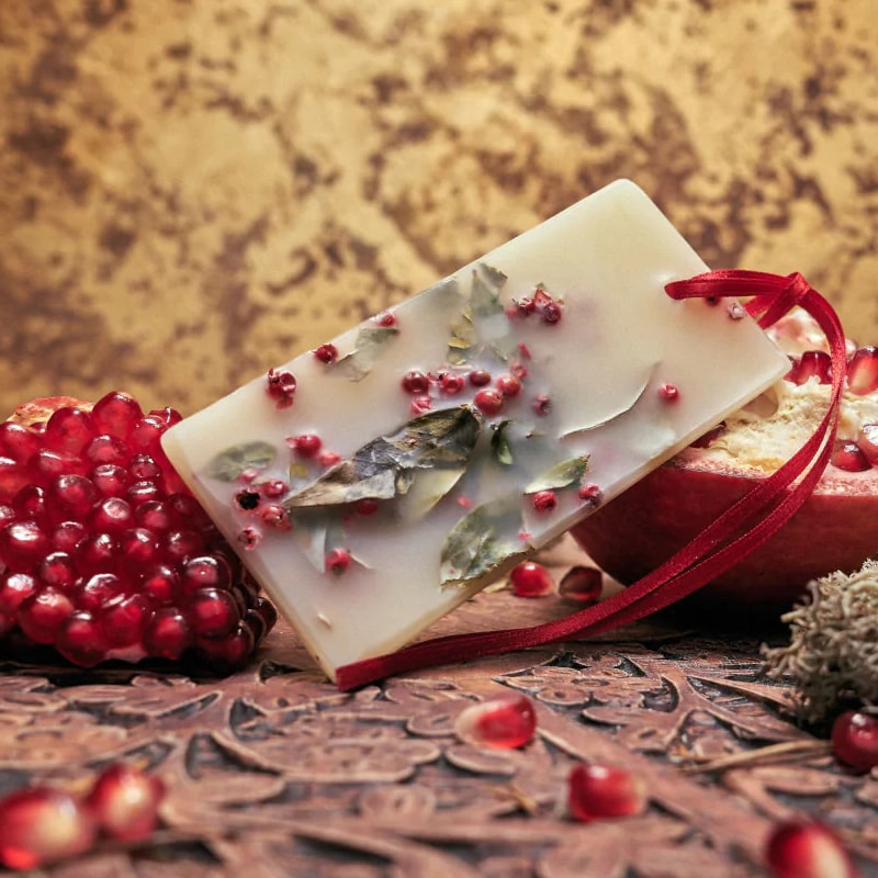 Lifestyle shot of Santa Maria Novella Melograno Scented Wax Tablet with pomegranate in the background