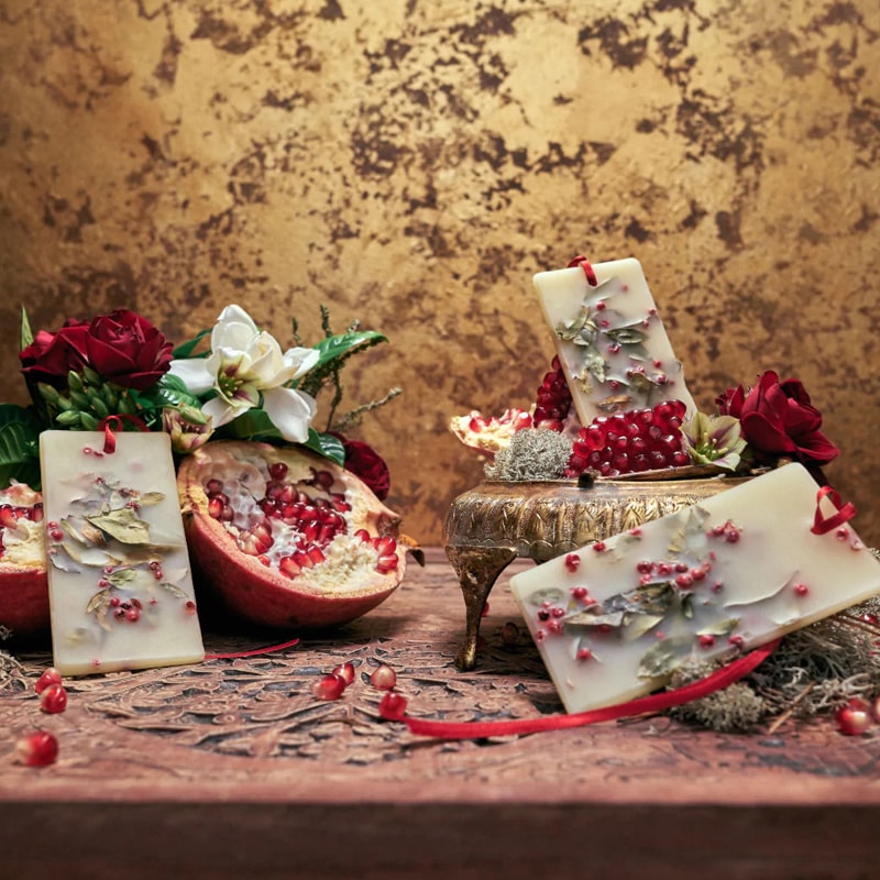 Lifestyle shot of Santa Maria Novella Melograno Scented Wax Tablets with pomegranate and red rose in the background