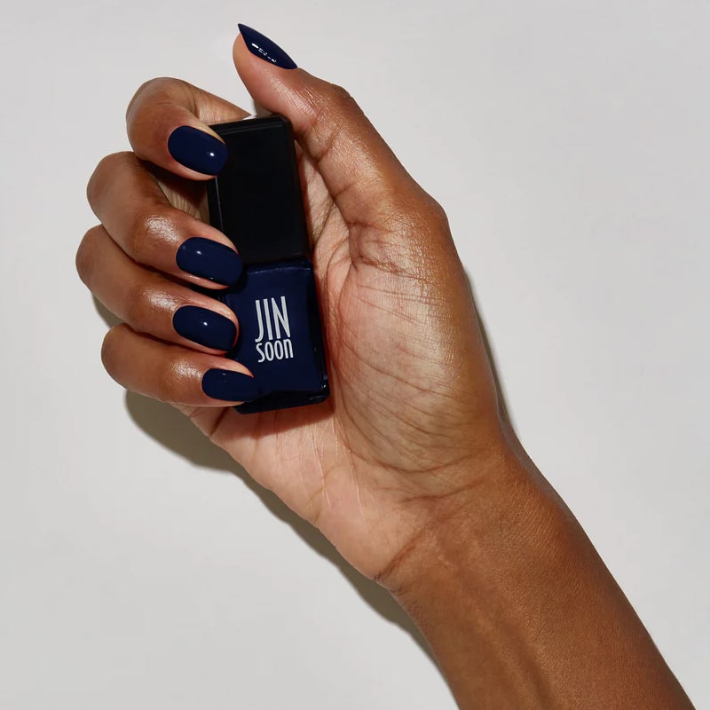 Model with dark skin tone wearing and holding bottle of JINsoon Nail Lacquer - Abyss