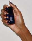 Model with dark skin tone wearing and holding bottle of JINsoon Nail Lacquer - Abyss