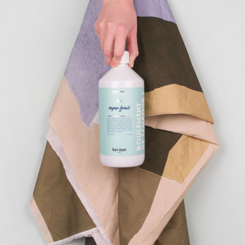 Lifestyle shot of model holding Kerzon Fragranced Laundry Soap - Super Frais (33.34 oz) with colorful blanket in the background
