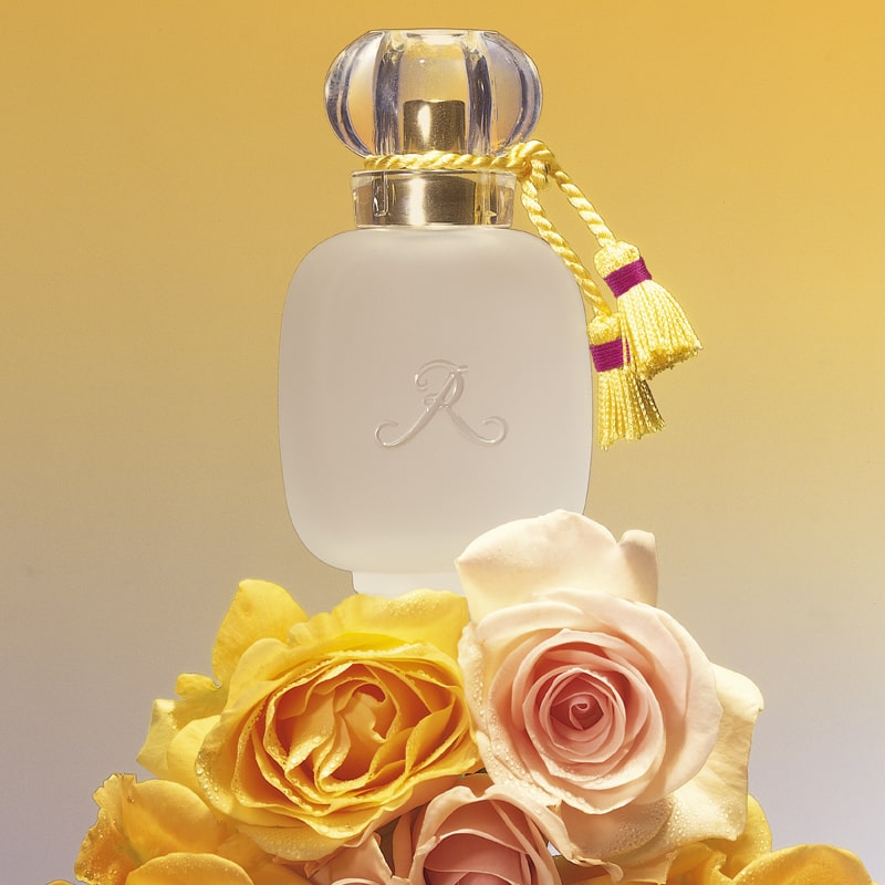 Les Parfums de Rosine Rose d&#39;Ete (100 ml) sitting on top of pale pink and yellow roses
