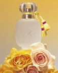 Les Parfums de Rosine Rose d'Ete (100 ml) sitting on top of pale pink and yellow roses