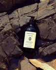 Lifestyle shot of Sangre de Fruta Botanical Hand Wash Neroli Noir (500 ml) top view with rocks and water in the background