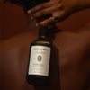 Lifestyle shot of Sangre de Fruta Botanical Shampoo Head of Roses (500 ml) held behind the back of model