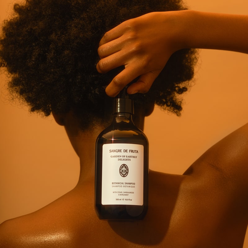 Lifestyle shot of model holding Sangre de Fruta Botanical Shampoo Garden of Earthly Delights (500 ml) bottle