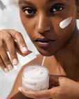 Caudalie Vinoperfect Instant Brightening Moisturizer shown on model's face and in her hand an open jar