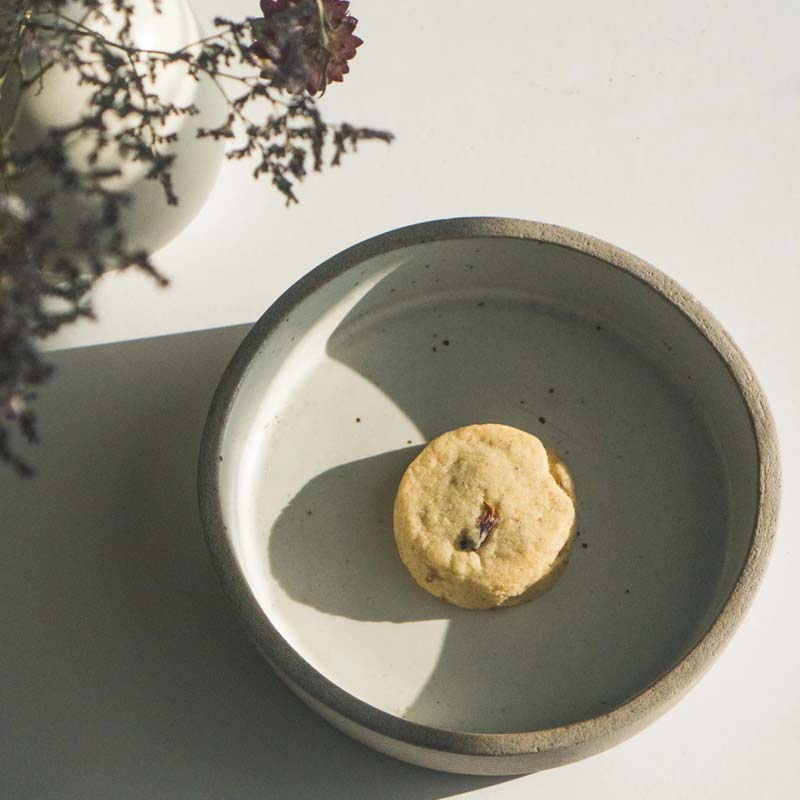 Lifestyle shot of Makabi &amp; Sons Rose Pistachio Cardamom Cookies - Maroc (one cookie shown without box in a dish)