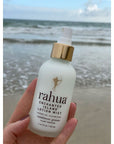 Rahua by Amazon Beauty Rahua Enchanted Island Lotion Mist held in front of the beach in background