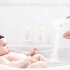 baby in bath with mother pouring in Bathorium Little Charlie Bath Soak