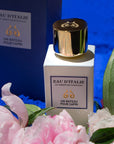 Lifestyle shot of Eau d'Italie Un Bateau Pour Capri Eau de Parfum Spray (100 ml) with box and pink flowers and green leaves in the foreground