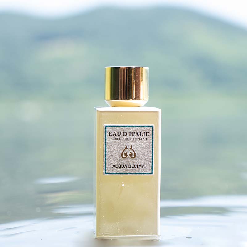 Lifestyle shot of Lifestyle shot top view of Eau d'Italie Acqua Decima Eau de Parfum Spray (100 ml) with lemon slices around the bottle sitting in water with mountainside in the background