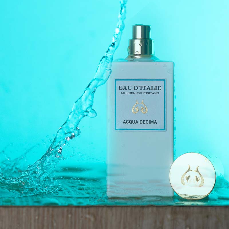 Lifestyle shot of Eau d'Italie Acqua Decima Eau de Parfum Spray (100 ml) on wood shelf with cap off, water splashing and bright blue background