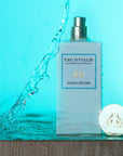 Lifestyle shot of Eau d'Italie Acqua Decima Eau de Parfum Spray (100 ml) on wood shelf with cap off, water splashing and bright blue background