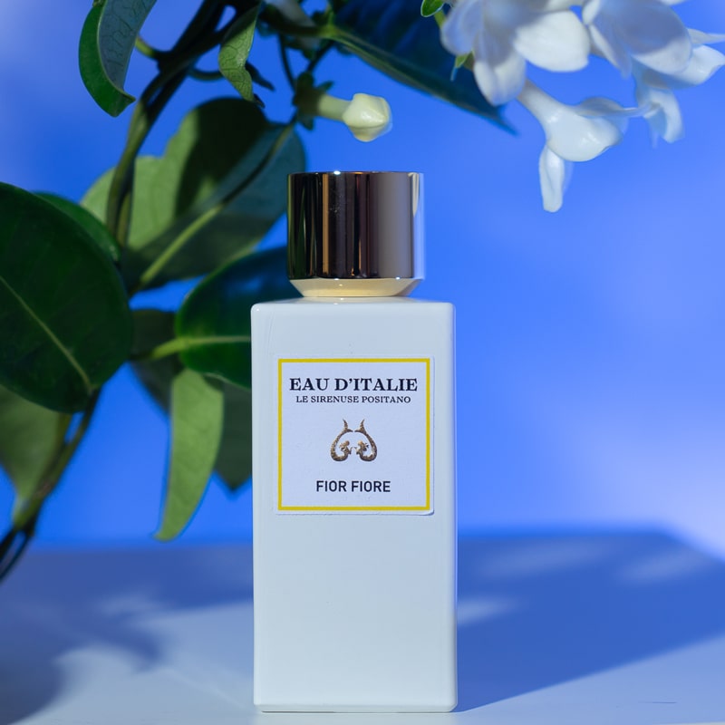 Lifestyle shot of Eau d'Italie Fior Fiore Eau de Parfum Spray (100 ml) with white flowers in the background