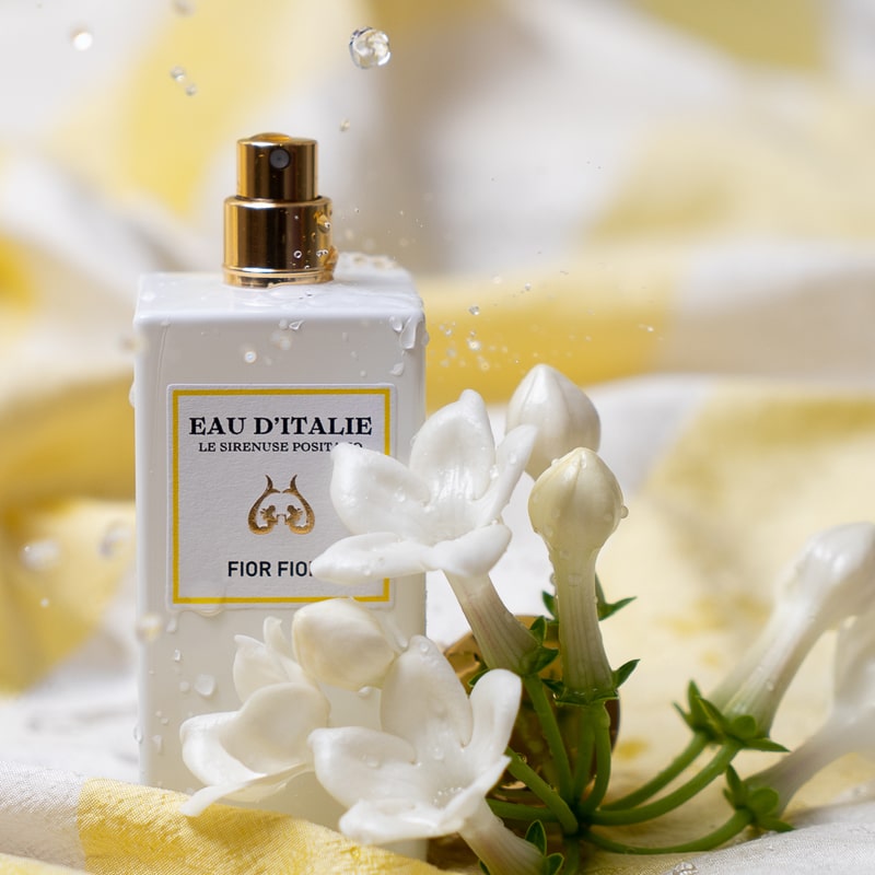 Lifestyle shot of Eau d'Italie Fior Fiore Eau de Parfum Spray (100 ml) with white flowers in the foreground and water splashing