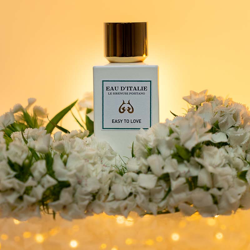 Lifestyle shot of Eau d&#39;Italie Easy to Love Eau de Parfum Spray (100 ml) with white flowers in the background and foreground