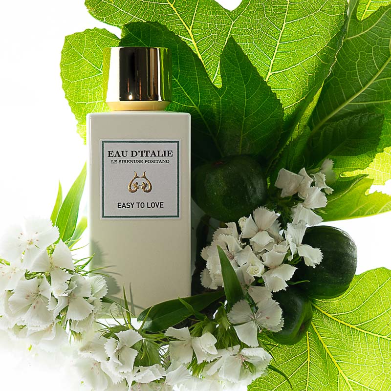 Lifestyle shot top view of Eau d'Italie Easy to Love Eau de Parfum Spray (100 ml) with white flowers and large green leaves in the background