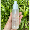 Athar’a Pure Moroccan Rose Toning Spray in model's hand in front of green plants