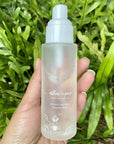 Athar’a Pure Moroccan Rose Toning Spray in model's hand in front of green plants