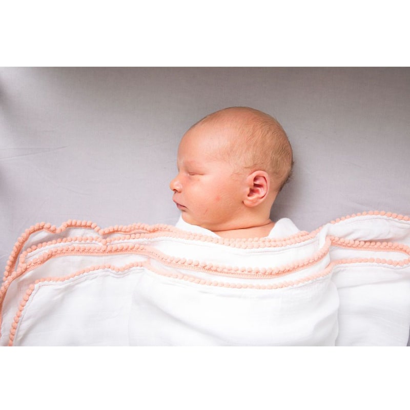 Luxe Silky Soft Bamboo Cotton Swaddle – Peach Pom Pom Trim shown across baby&#39;s chest (baby not included)