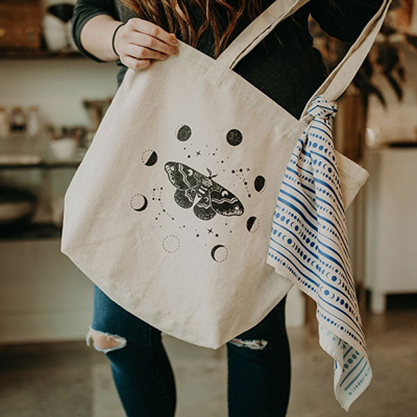 Mineral and Matter Moth and Moons Tote Bag - shown in model's hands with a scarf tied for flair (not included)