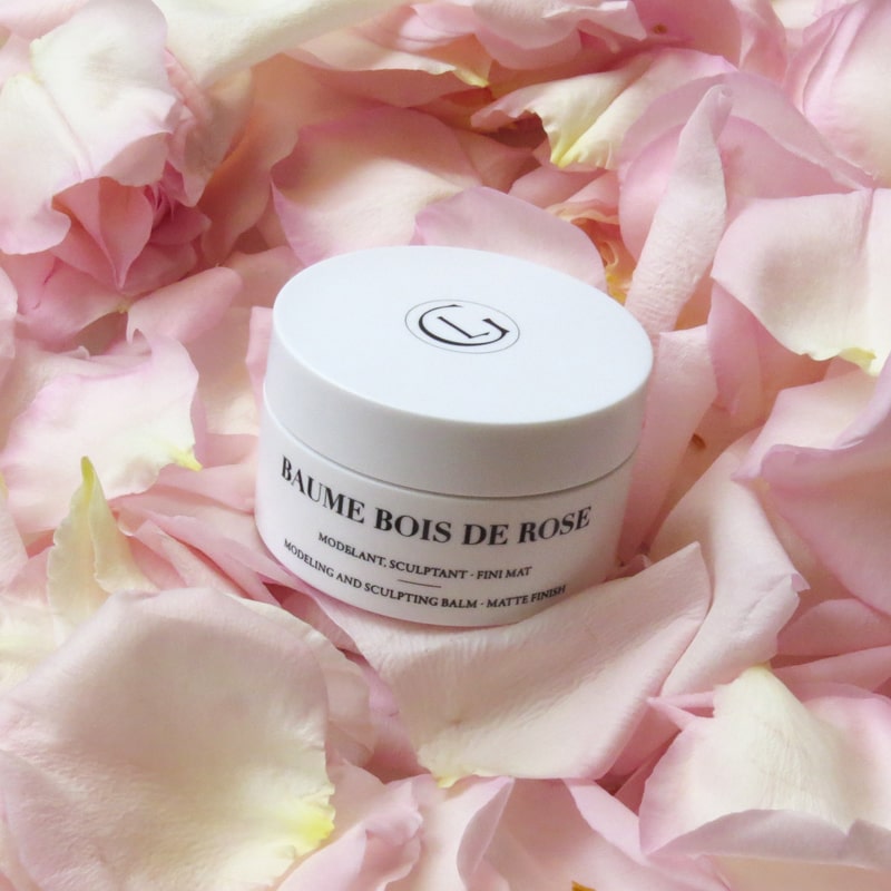 Lifestyle shot of Leonor Greyl Baume Bois de Rose shown with petals in background