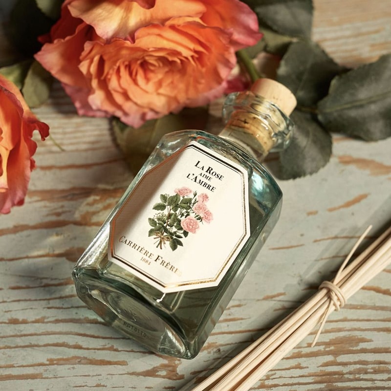 Lifestyle top view shot of Carriere Freres Rose Amber Diffuser shown with diffuser sticks and roses in background