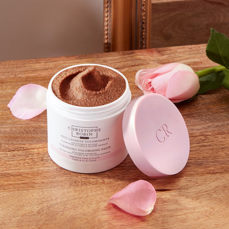 Christophe Robin Cleansing Volumizing Paste with Pure Rassoul Clay and Rose Extracts beauty shot of an open jar on a table with rose and petals