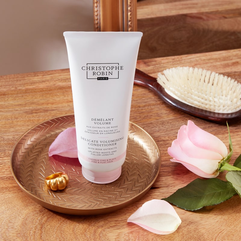 Christophe Robin Delicate Volume Conditioner with Rose Extracts lifestyle shot showing tube on a tray with rose and a hairbrush