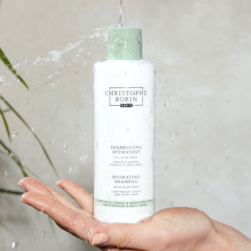 Christophe Robin Hydrating Shampoo with Aloe Vera shown in model&#39;s hand with water pouring on it