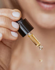 Olverum Pure Radiance Facial Oil showing model holding dropper and squeezing out a drop