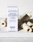 OJOOK Silk Floss Refill lifestyle shot showing several rolls of floss beside box (sold individually)