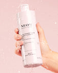 Neom Organics Super Shower Power Body Cleaner in model's hand with water splashing on it
