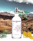 Lifestyle shot of Cinq Mondes Eau de L’Atlas Fresh Aromatic Mist (3.4 oz) with mountain landscape in the background and illustrations of ingredients in the foreground