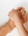 Blu Kat Kids Rose Quartz Bracelet shown on child model's wrist atop mother's wrist wearing jade bracelet