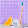 Cocolab Cocobrush Pedestal - lifestyle shot showing a cocobrush in the pedestal with floss beside and an orange slice with purple tile in background
