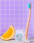 Cocofloss Cocobrush Pedestal - lifestyle shot showing a cocobrush in the pedestal with floss beside and an orange slice with purple tile in background