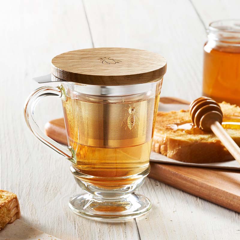 La Rochere Bee Tea Infuser Mug - lifestyle shot showing mug with tea in it and toast with honey in background
