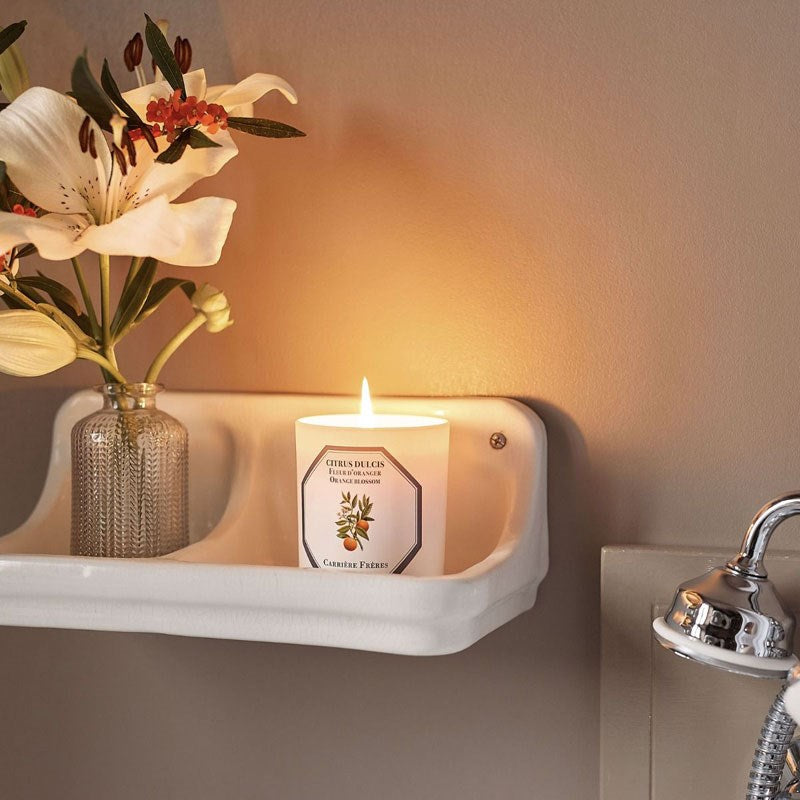 Carriere Freres Orange Blossom Candle showing lit candle in bathroom setting beside a floral arrangement