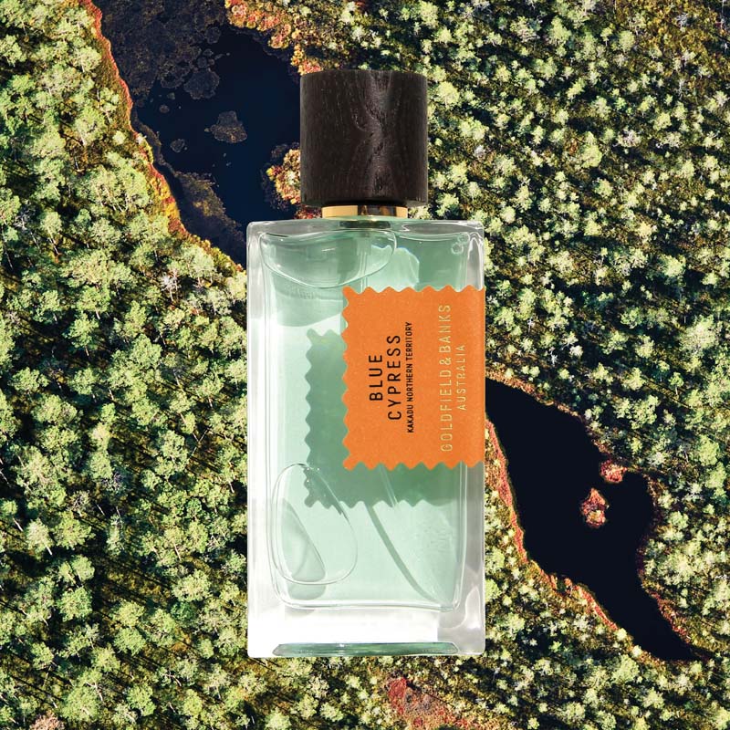 Mood shot of Goldfield &amp; Banks Blue Cypress Perfume 100 ml with aerial view of water and green trees in the background