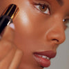 Roen Beauty Roglow Skin Stick Highlighter – Lit showing model putting product on cheek
