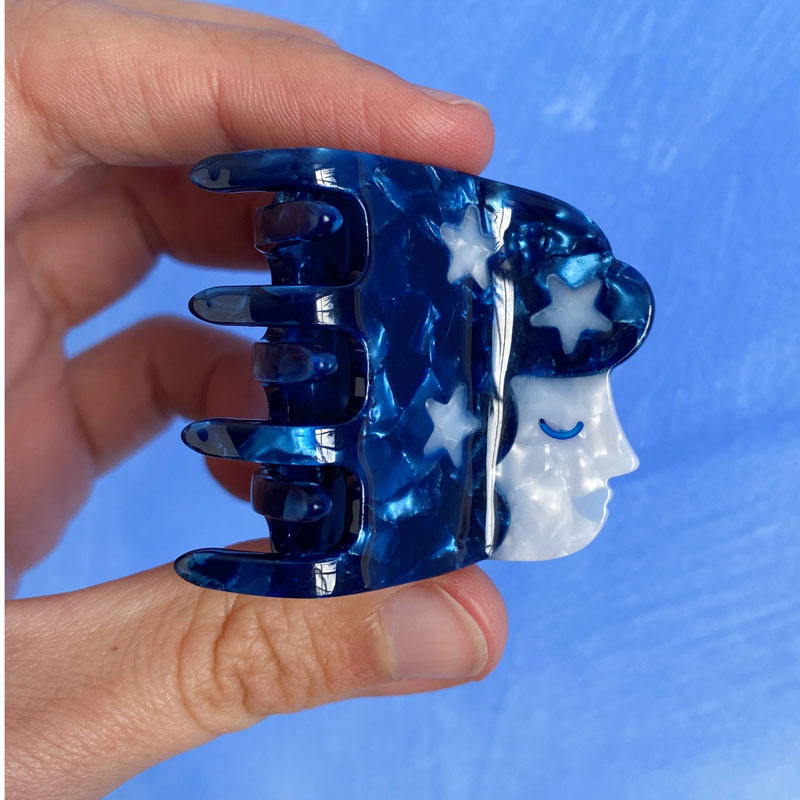 Lisa Junius Starry Girl Hair Claw showing in models hands, blue clip with stars and face