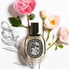 Diptyque Eau Rose De Parfum showing sitting in front of flowers